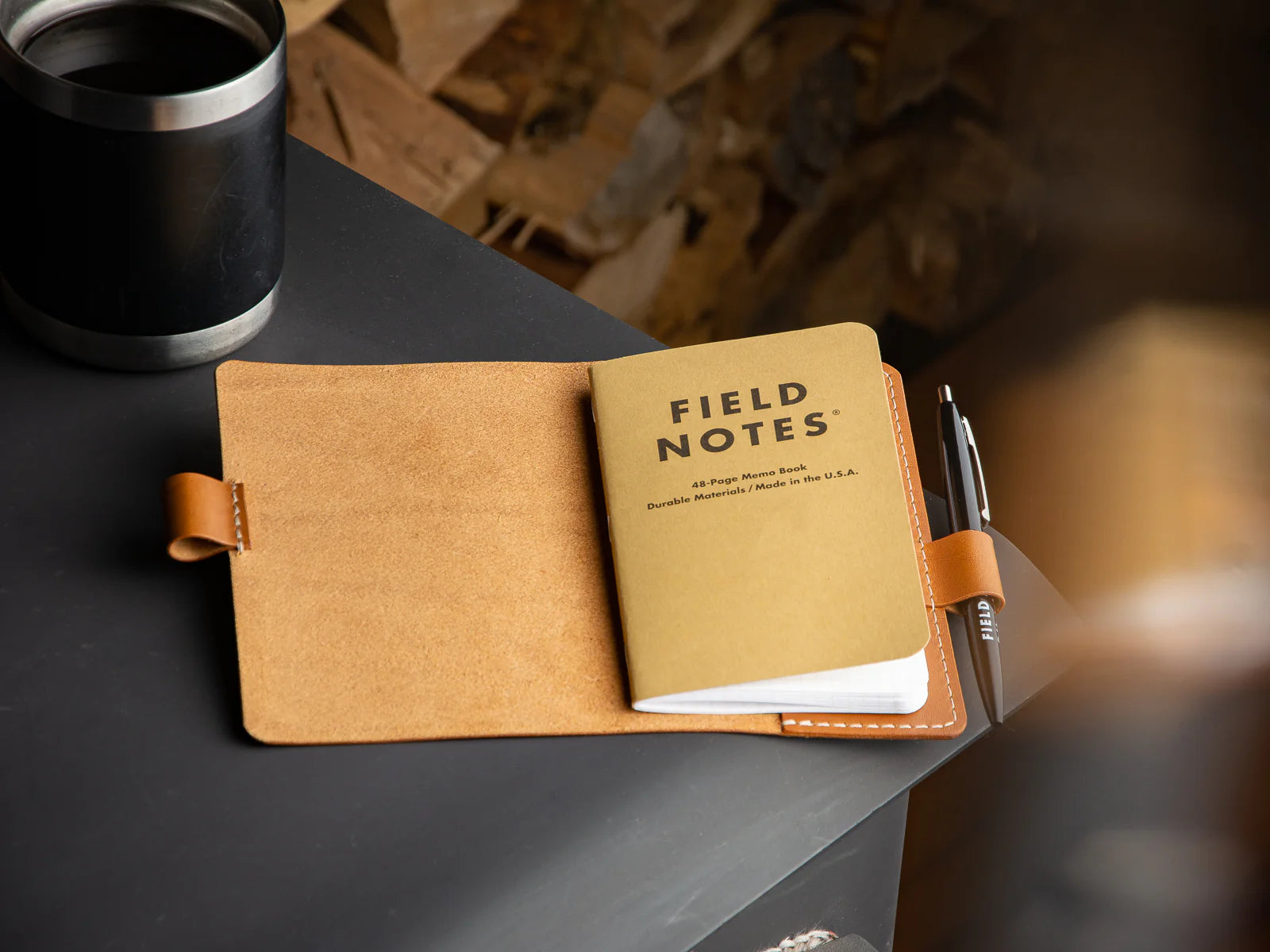 Open field notes notebook with a pen on a dark surface, blurred background