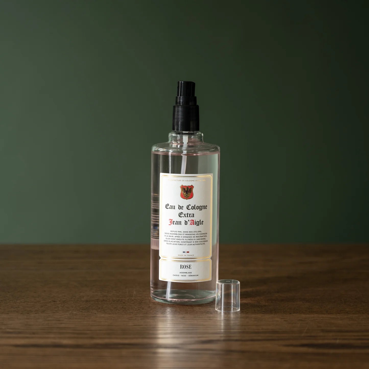 Clear Jean d'Aigle cologne bottle with a label on a wooden surface and green background