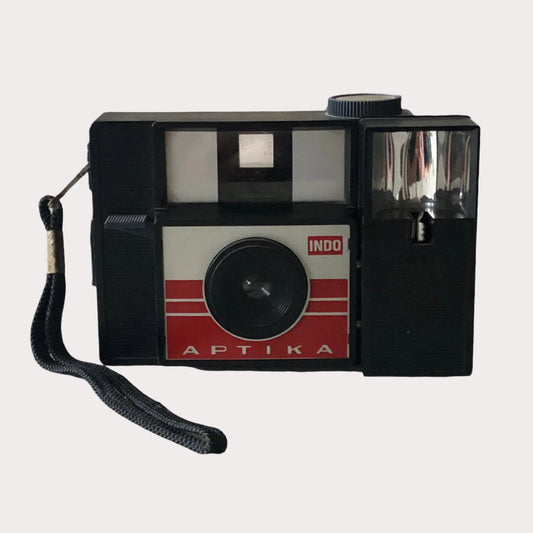 A vintage 1960s Fex Indo Aptika camera with a black body, white and red detailing, and a visible lens.